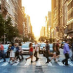 People crossing a busy city street at sunset