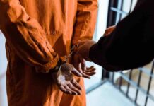 Garfield County Stunner: Five Felonies Prisoner in orange jumpsuit handcuffed by officer