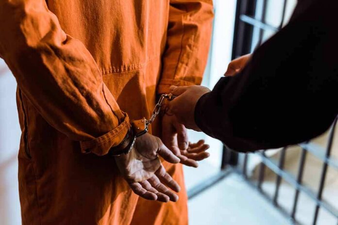 shutterstock_1036220185-1 Prisoner in orange jumpsuit handcuffed by officer