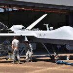 Military drone being serviced by ground crew outside a hangar