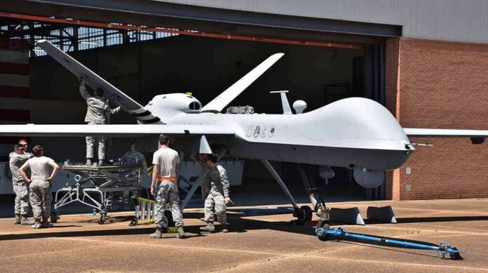 Military drone being serviced by ground crew outside a hangar