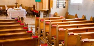 Empty wooden church pews with red hymnals