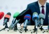 microphones clustered on a table at a press conference