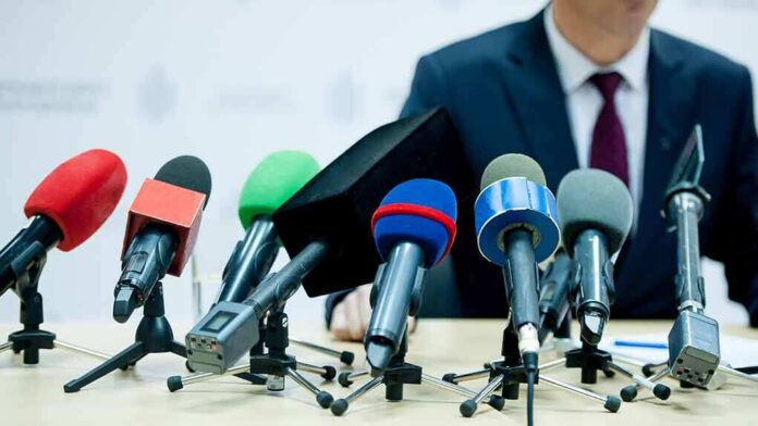 shutterstock_1245040021-1 microphones clustered on a table at a press conference