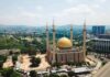 Golden-domed mosque with four minarets in a modern cityscape