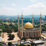 Golden-domed mosque with four minarets in a modern cityscape