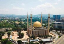 Golden-domed mosque with four minarets in a modern cityscape