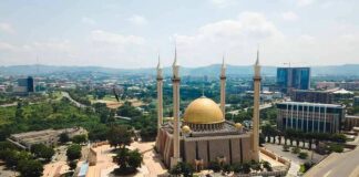 Golden-domed mosque with four minarets in a modern cityscape