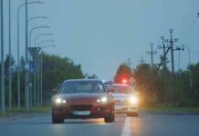 red car driving on road with police car behind using flashing lights