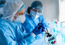 Scientists in protective gear working with a syringe in a laboratory