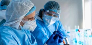 Scientists in protective gear working with a syringe in a laboratory