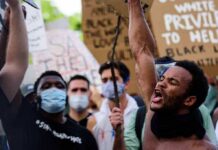 Protester shouting with raised fist amid crowd holding signs