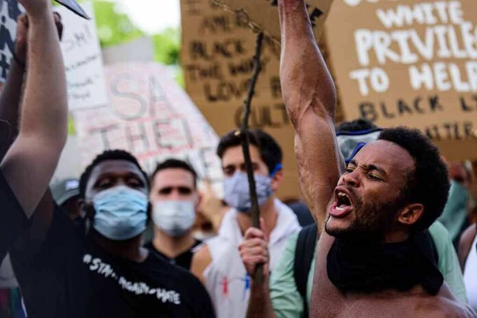 shutterstock_1751099579-2 Protester shouting with raised fist amid crowd holding signs