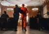 Prisoner in orange jumpsuit escorted by officer in a courtroom