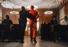 Prisoner in orange jumpsuit escorted by officer in a courtroom
