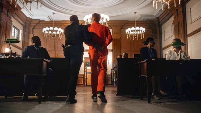 Prisoner in orange jumpsuit escorted by officer in a courtroom