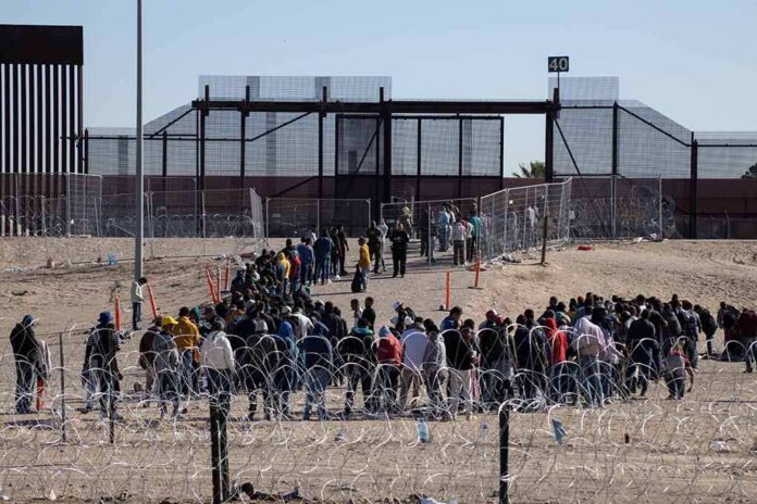 shutterstock_2307918121-4 Crowd of people lining up near a border fence with barbed wire