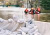 Sandbags stacked near a flooded street with rescue workers in a boat