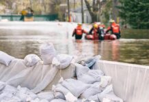 Sandbags stacked near a flooded street with rescue workers in a boat