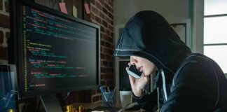 Person in hoodie using computer and phone at desk
