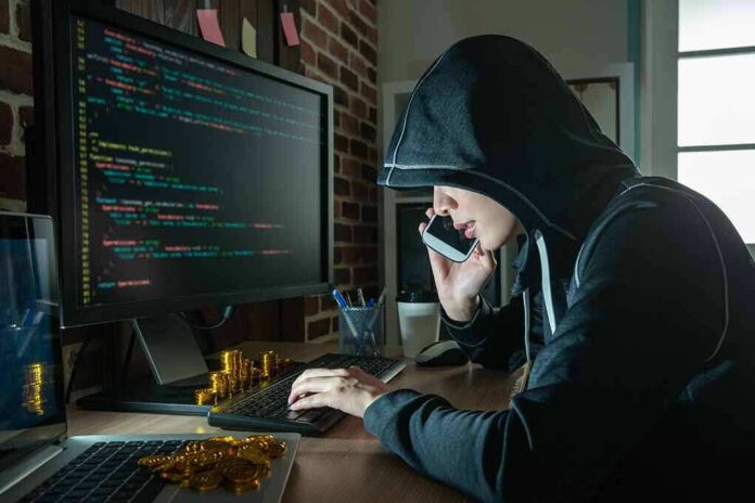 Person in hoodie using computer and phone at desk
