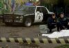 Crime scene with police car and two investigators by a covered body