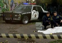 Crime scene with police car and two investigators by a covered body
