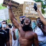 America’s Lynching History Still Shapes Today Shirtless protester raises fist while crowd holds signs