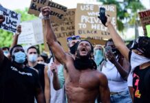 Shirtless protester raises fist while crowd holds signs