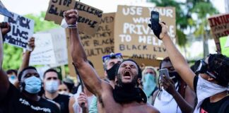 Shirtless protester raises fist while crowd holds signs
