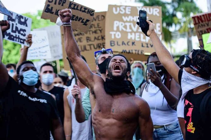 Shirtless protester raises fist while crowd holds signs
