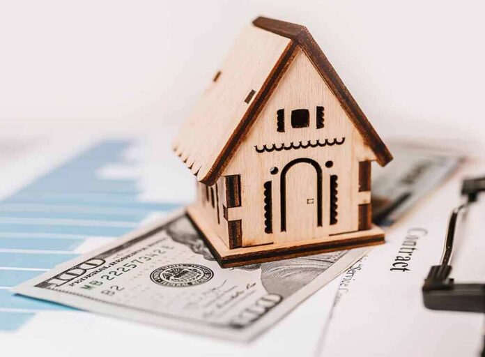 shutterstock_1899778699-1 Wooden house model on money and contract papers
