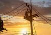 Utility workers on power poles at sunset