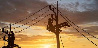 Utility workers on power poles at sunset