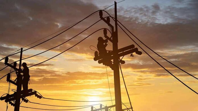 shutterstock_1979642963-11 Utility workers on power poles at sunset