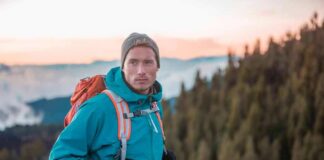 Hiker in teal jacket with backpack at mountain viewpoint