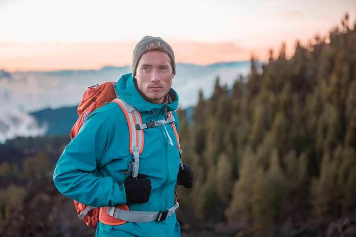 shutterstock_2017966631-1 Hiker in teal jacket with backpack at mountain viewpoint