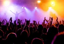 Macklemore Dispute Tests Limits of Venue Power Crowd at a concert with raised hands and colorful stage lights
