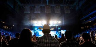 Cowboy-hatted man watches a concert in a packed arena