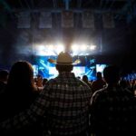 Cowboy-hatted man watches a concert in a packed arena