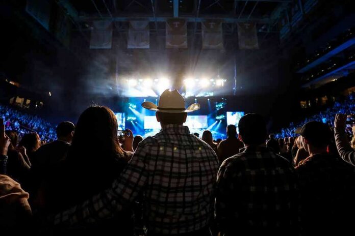 shutterstock_2150018925-3 Cowboy-hatted man watches a concert in a packed arena