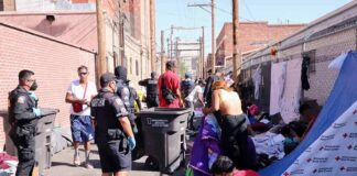 Police officers interact with people in an alley encampment