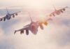 Three fighter jets flying in formation above clouds at sunrise