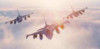Three fighter jets flying in formation above clouds at sunrise