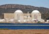 Nuclear power plant with domed structures beside a water body and mountains in the background