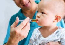 Baby taking liquid medicine from an oral syringe held by an adult