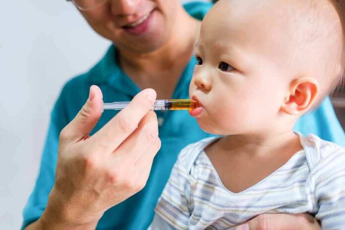 shutterstock_602417219-5 Baby taking liquid medicine from an oral syringe held by an adult