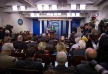 Press secretary at podium addressing reporters in briefing room