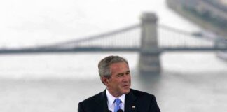 George W. Bush speaking at a podium with a bridge over water in the background