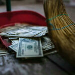 Inside a $1.6 Billion Venezuelan Money Trail Broom sweeping dollar bills into red dustpan floor